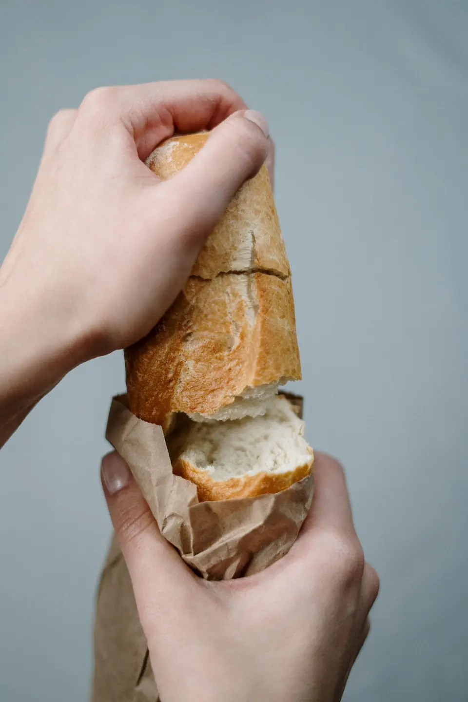 Hands breaking a baguette out of a brown paper bag