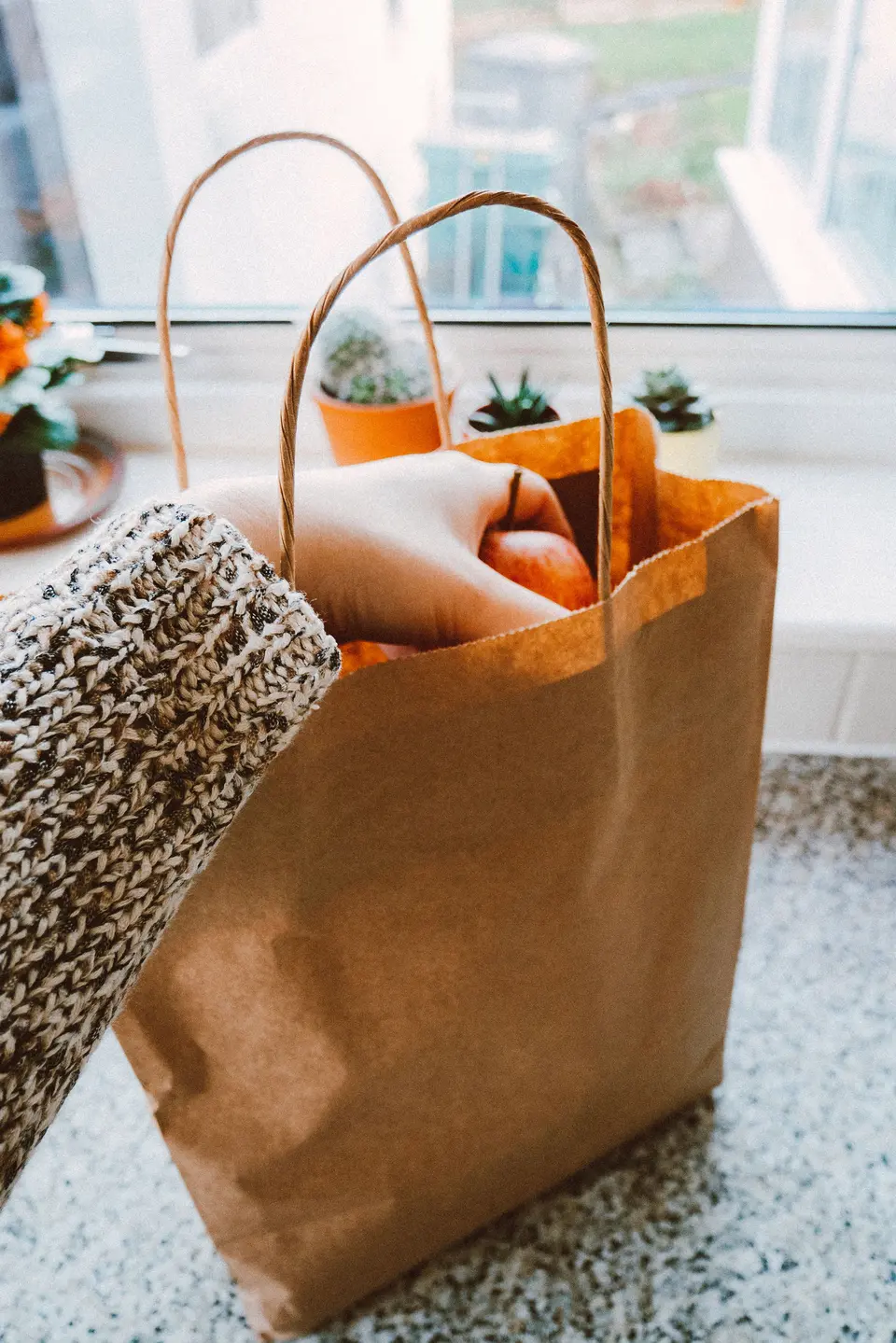 A kraft bag with twisted handles on a counter, a hand reaching in