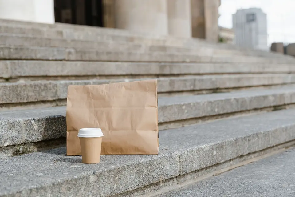 A plain kraft paper bag and a kraft coffee cup on stone steps
