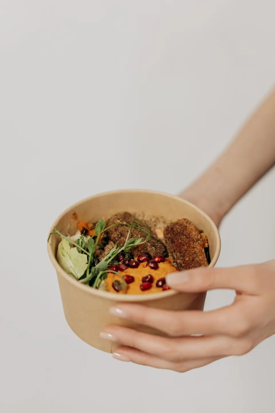 Hands holding a round kraft paper bowl filled with a grain bowl