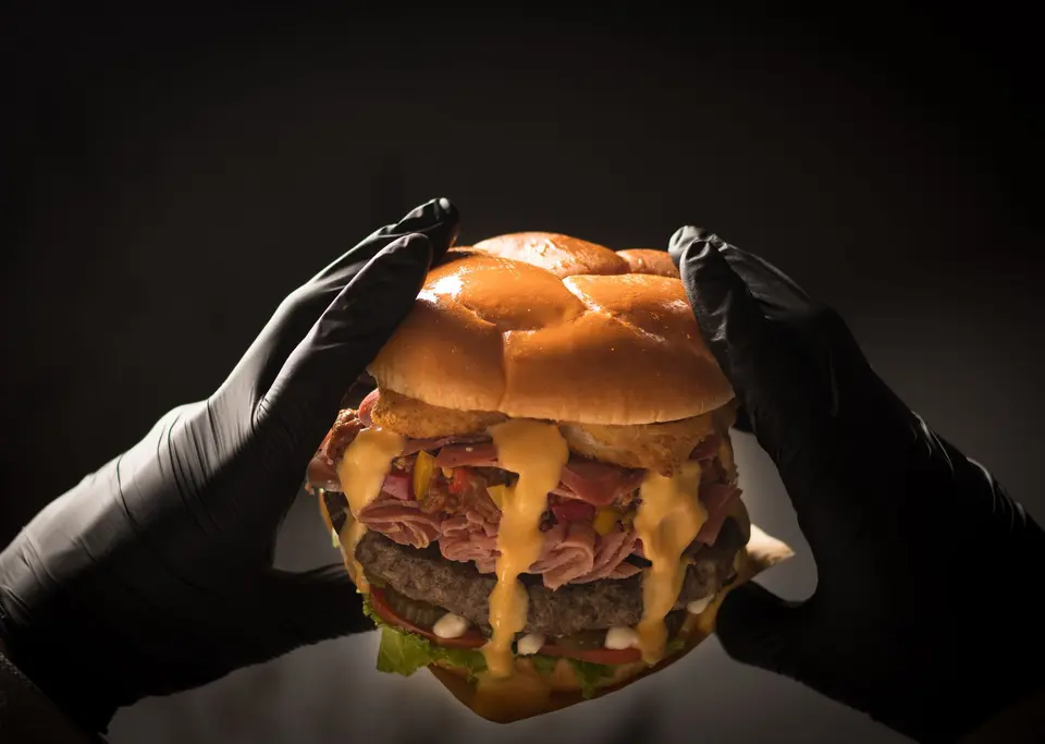 Cook in black gloves holding a tall cheeseburger