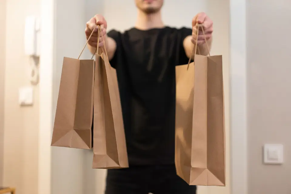 A person holding out two kraft paper bags with twisted handles