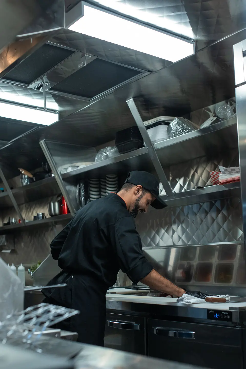 A cook wiping down the steel counter inside a food truck kitchen