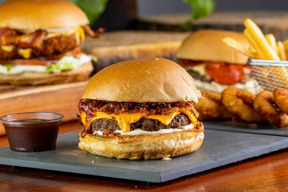Cheeseburger with bacon on a slate board, onion rings and fries behind it