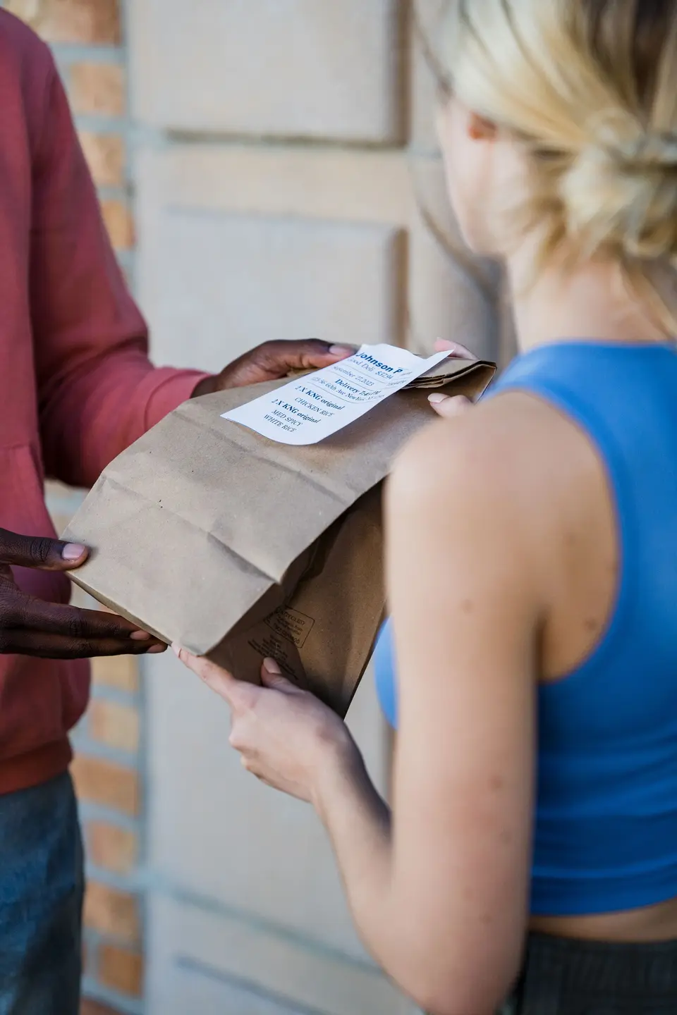 Courier handing over a kraft paper takeout bag with the order ticket on it